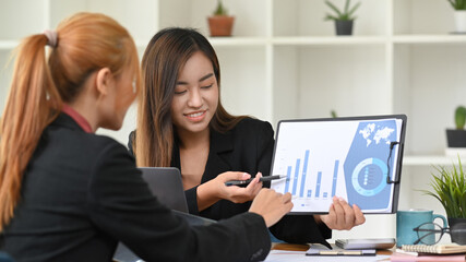 Two business women analyzing marketing research reports together at office desk