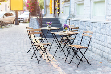 Empty cafe with terrace with tables and chairs. Street exterior of  restaurant. Flowers in vase on table. Furniture for coffee shop in street in Europe in summer. Old Cozy street with tables of cafe