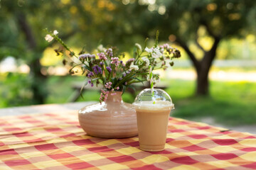 Cold iced coffee with milk on table. Cold summer drink in garden. Caramel frappe coffe in street coffee shop. Bouquet of summer flowers in ceramic vase on terrace. Cozy home decor of patio yard
