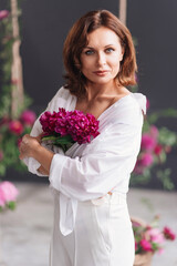a gentle middle-aged woman in white clothes with a bouquet of peonies