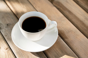White ceramic coffee cup on the old wooden floor with the morning sun.