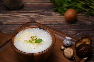 Rice porridge with soft boiled egg, slice ginger and scallion in wooden bowl. Congee is a type of rice porridge popular in many Asian countries