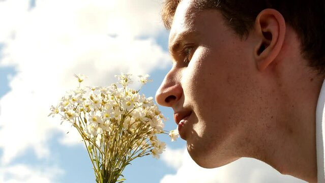 Young man smelling white field flowers in hand and sky with clouds. Pavel, i and field flowers, side view. Date of shooting day 5 June 2022 year, MSK time. This video was filmed in Russia.