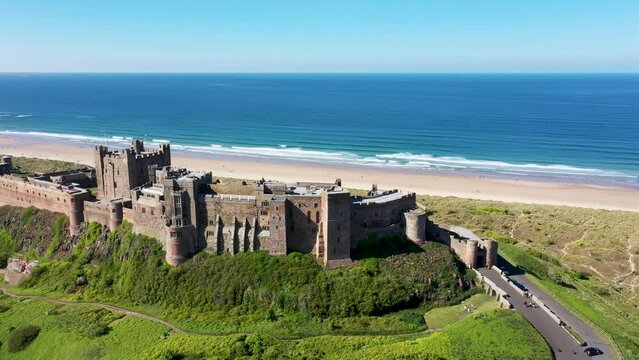 Aerial footage the famous Bamburgh Castle, a castle on the northeast coast of England, by the village of Bamburgh in Northumberland showing a drone view of the castle and sandy beach in the summer.