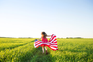 US Independence Day or Memorial Day. patriotic background with copy space. child girl with American flag runs back across field in nature.