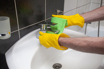 Male hands in yellow gloves cleaning sink and faucet