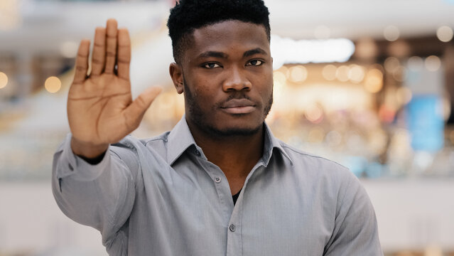 Close-up of young serious confident african american man looking at camera puts forward palm showing stop gesture demonstrating protection personal boundaries protest against violence racism refusal