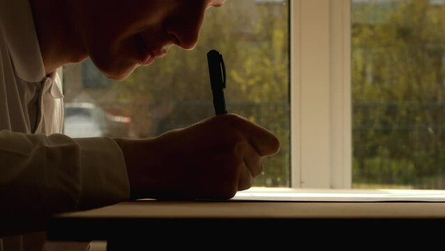 Young artist Pavel write author signature on drawing with heptagon on paper, side view. Date of shooting day 10 May 2022 year, MSK time. This video was filmed in Russia.