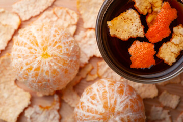 Two peeled tangerines near cup of hot tea with some added peel. Adding tangerine peel to tea