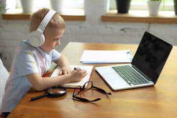 One cute little boy, school age kid listening online lesson, using laptop at home interior. Education, childhood, people, homework and school concept.