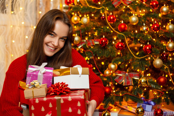 Fototapeta na wymiar Laughing girl with a pile of presents near Christmas tree. Happy female received many presents at Christmas, showing them to the camera