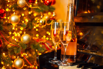 Bottle of white wine and two wineglasses full of drink on the piano with background of Christmas tree. Celebrating Christmas or New Year with a partner, romance concept
