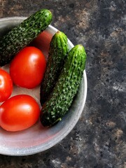 Cucumber and tomato. Fresh vegetables in a rustic metal plate on a black concrete background. Summer salad ingredients.