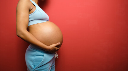 Side view detail of sporty pregnant woman belly on red wall background for copy space. - obrazy, fototapety, plakaty