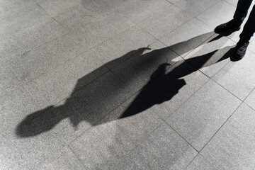 Dark shadow of a lonely person on the ground in the street. Stranger with a cigarette. Anxiety,...