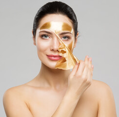 Beauty Woman peeling off Golden Facial Mask. Smooth Skin Model taking off Gold Purifying Face Film Mask over Gray. Women cleansing Cosmetics and Skincare Cosmetology - obrazy, fototapety, plakaty