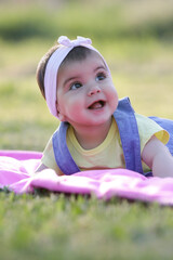 Happy baby girl laying on the grass during summer day	