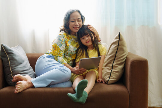 Asian portrait, Grandma and granddaughter doing recreational activities playing tablet computers on the sofa