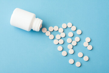 White plastic bottle and pills on blue background.