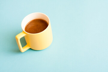 Simple concept yelow cup of fresh hot coffee on blue background.