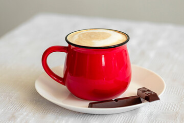 Red cup of cappuccino and chocolate on the table close-up. Food photo.
