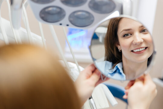 young woman smiling with healthy white teeth, looking in dental mirror