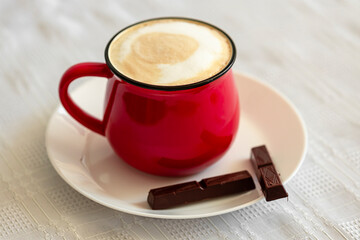 Red cup of cappuccino and chocolate on the table close-up. Food photo.