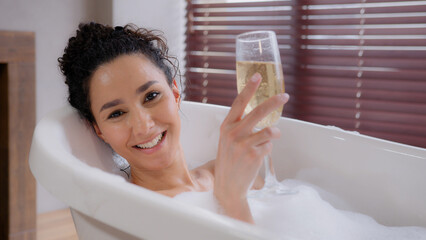 Close-up young happy relaxed woman relaxes in foam bath drinking wineglass champagne enjoys fragrant drink enjoying luxury bathroom romantic girl taking bathtub with bubbles smiling resting relaxing