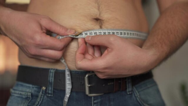 Adult man hands measure fat belly with tape measure. Overweight man torso without T-shirt. Tape measure around man fat belly on blurred background extreme closeup