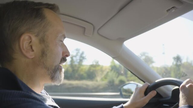 A middle-aged handsome Caucasian man drives a car on a highway - side closeup