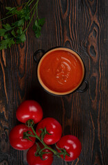 Tomato soup in a black bowl on brown background. Top view.