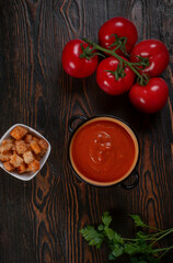Tomato soup in a black bowl on brown background. Top view.