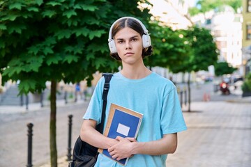 Serious teenage male student with textbooks looking at camera outdoor