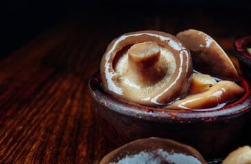 Beautiful delicious pickled mushrooms in a clay cup on a wooden table .