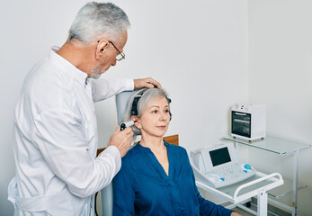 Mature audiologist with tympanometer probe doing procedure tympanometry or impedance audiometry for...