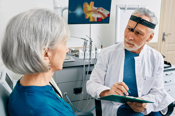 Obraz premium Grey-haired doctor doing consultation for senior woman patient with health problems at ENT center. ENT doctor's consultation
