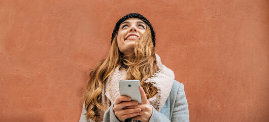 Blonde girl with a smartphone looks up with positivity and happiness