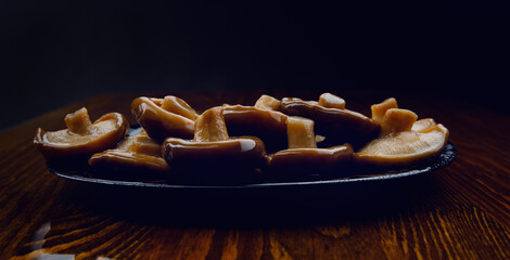 A scattering of pickled mushrooms in a black plate . Healthy village food . Pickled black milk mushroom .