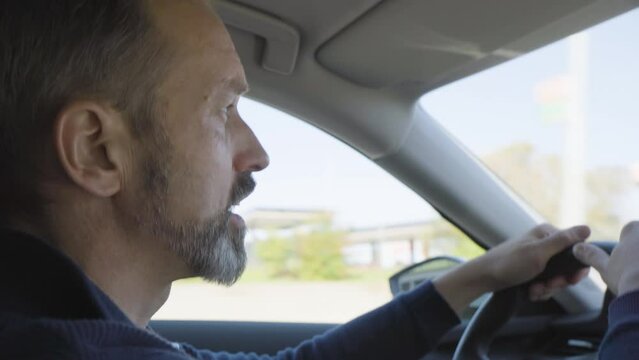 A middle-aged handsome Caucasian man acts angry in a road rage as he drives a car on a highway - side closeup