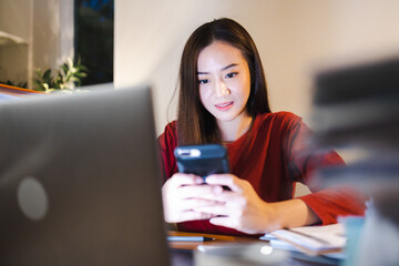 Happy Female Accountant using smart phone during overtime at home at night