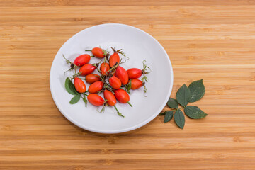 Red rose hips on white saucer on a wooden surface
