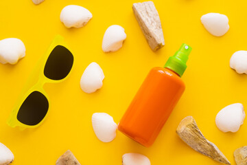 Top view of sunblock near seashells and sunglasses on yellow background.