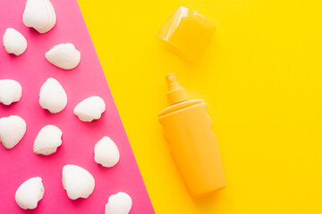 Top view of seashells and sunblock on pink and yellow background.