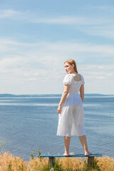 A beautiful girl stands on benches on the seashore with a view of the sky