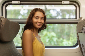 Travel and exploration of cheerful tourist woman by train in first class wagon to famous places of the country. Romantic smiling young traveler woman enjoying comfortable train ride, looking at the