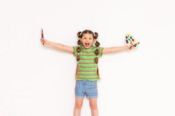 Children's creativity. A little girl was waving her arms in different directions with a palette of paints and brushes and smiling and shouting. White isolated background.