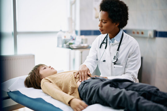 Black Female Doctor Examining Boy's Abdomen During Appointment At Medical Clinic.