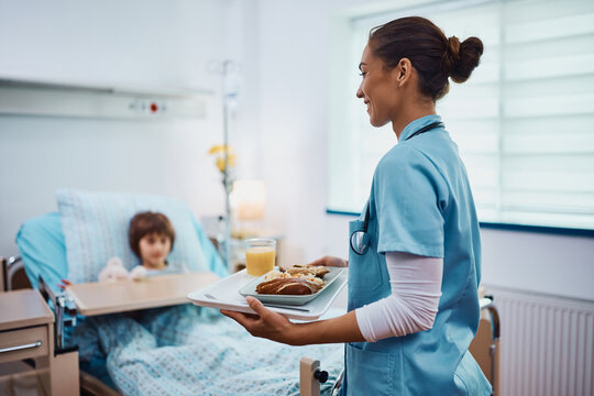 Young pediatric nurse serving lunch to a child at hospital ward. - Powered by Adobe