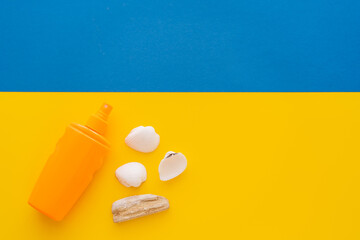 Top view of sunscreen near seashells on yellow and blue background.