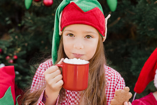 Merry Christmas. Portrait of funny child girl in Santa hat eating gingerbread cookies drinking hot chocolate outside having fun. Happy Holidays. kid enjoying holiday. Christmas in July
